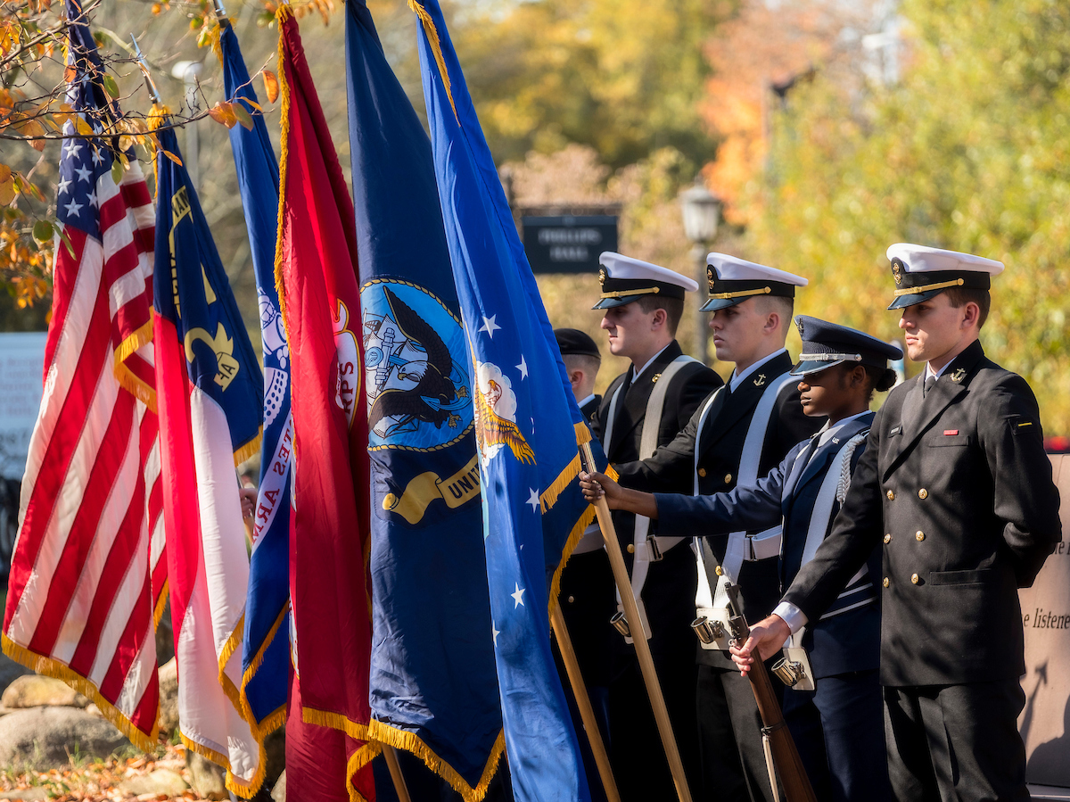U.N.C. student cadets hold flags and stand at attention.
