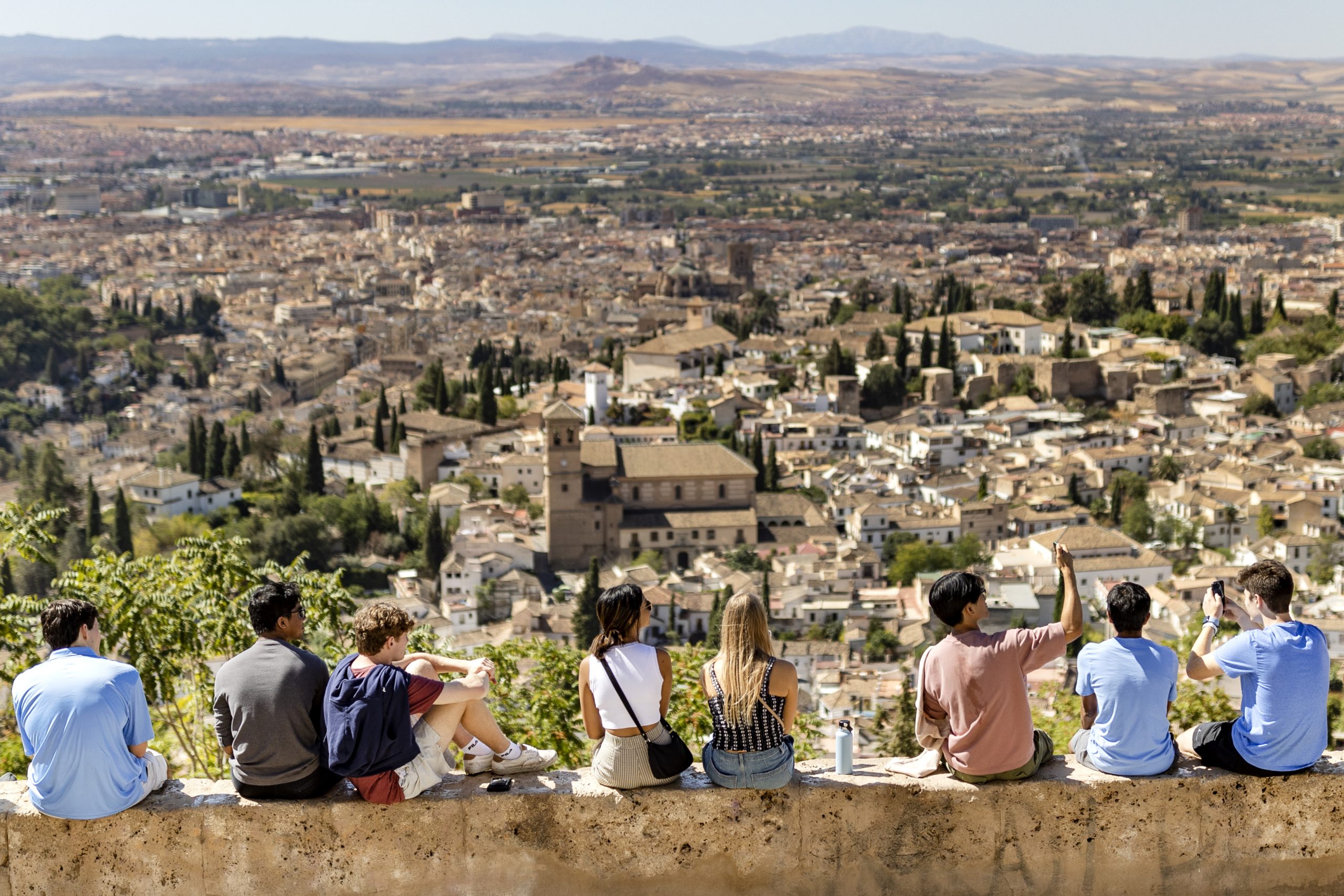 Students sitting on a wall with spain in the background.