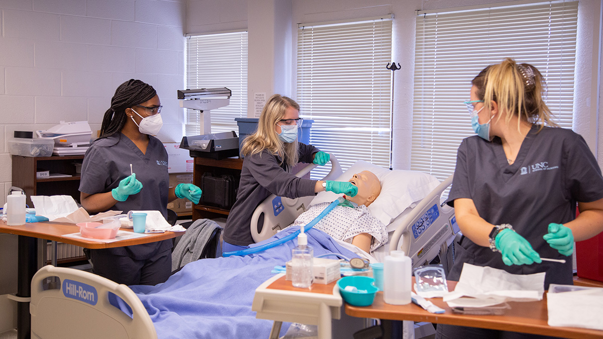Three students working on a practice dummy in a hospital bed.