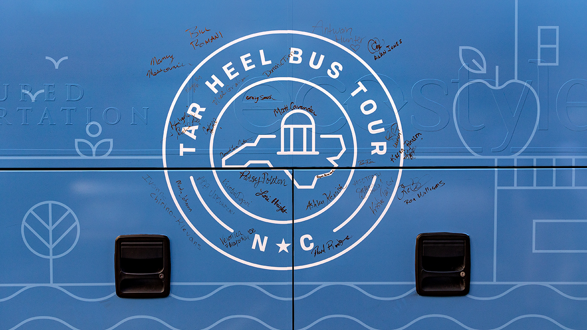The side of a Carolina Blue tour bus with the Tar Heel Bus Tour logo and signatures surrounding it.